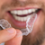 Close-up of a person holding a clear dental aligner near their smile.