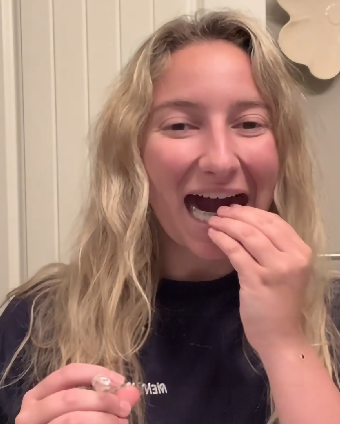 A smiling woman with wavy blonde hair eating a snack.