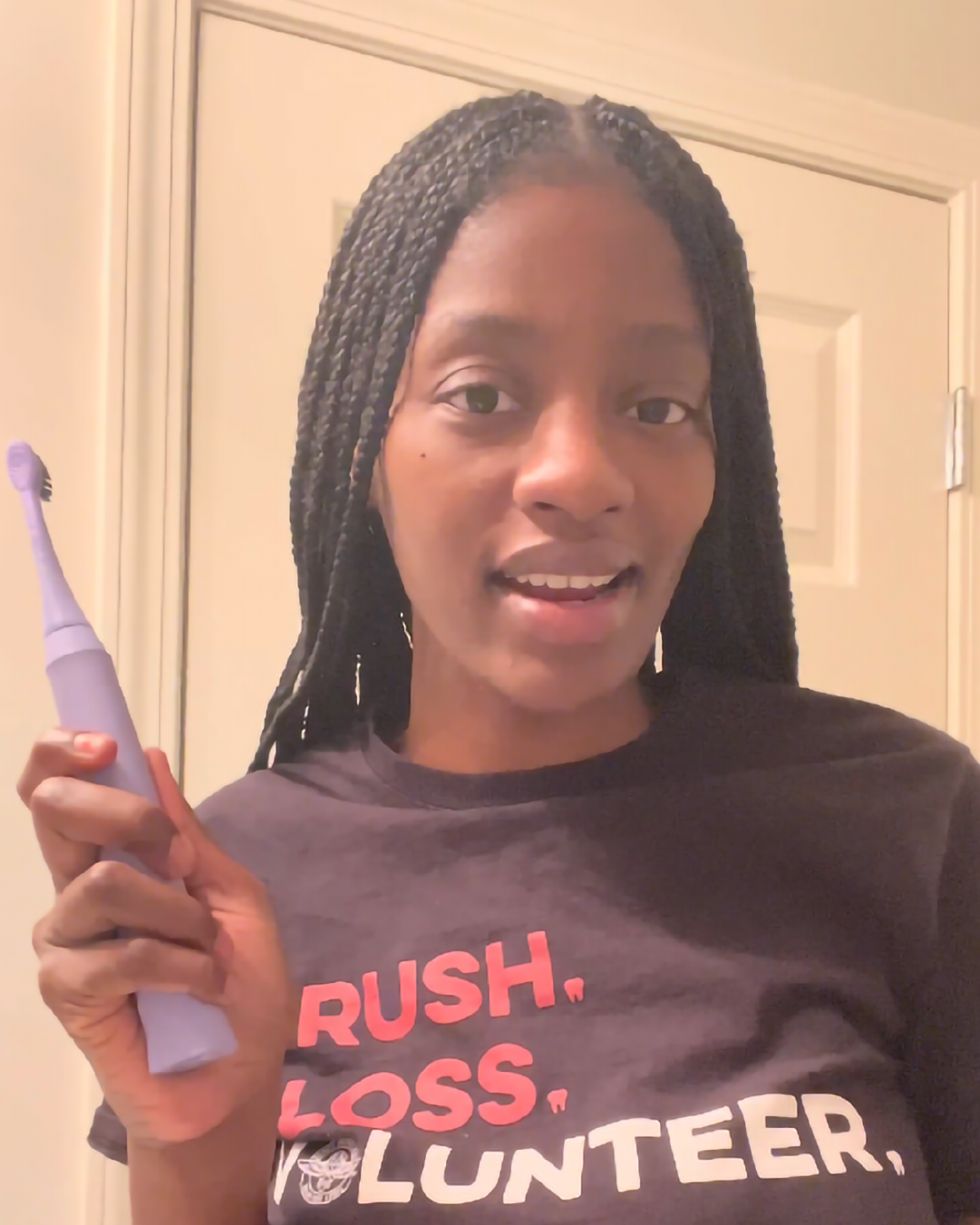 A person holding an electric toothbrush and wearing a t-shirt with the text "rush, loss, volunteer.