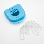 A blue plastic case labeled remi is shown next to two clear, comfortable retainers on a white background.