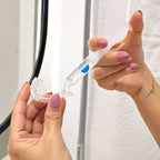 A person applies CP gel from a syringe onto a clear whitening tray, likely as a home whitening solution. The background shows a white wall and part of a mirror.