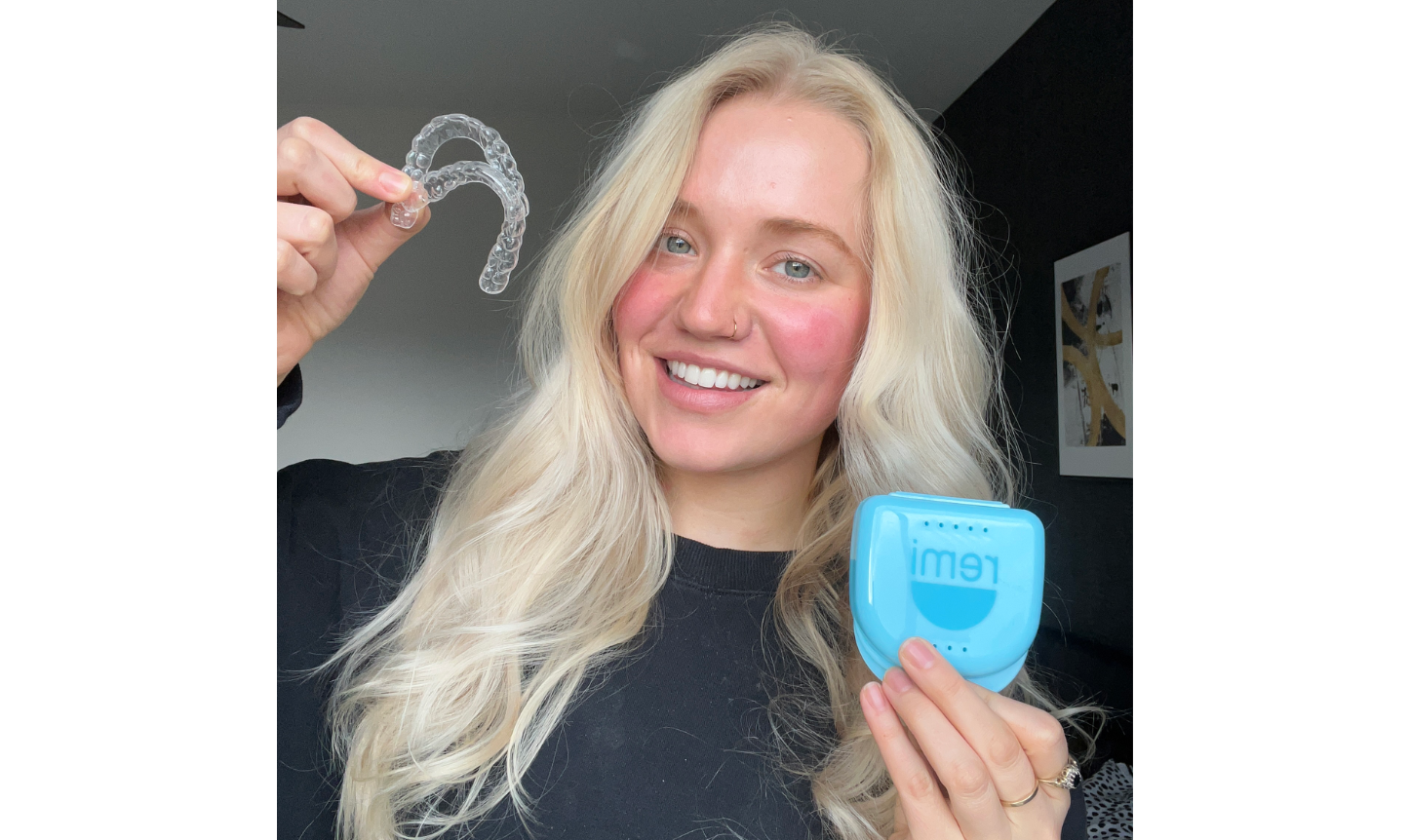 Woman holding an invisalign aligner and its case, smiling at the camera.