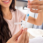 A woman applies teeth whitening gel from a syringe into custom trays, preparing them for overnight whitening. She is smiling and wearing a light pink shirt.