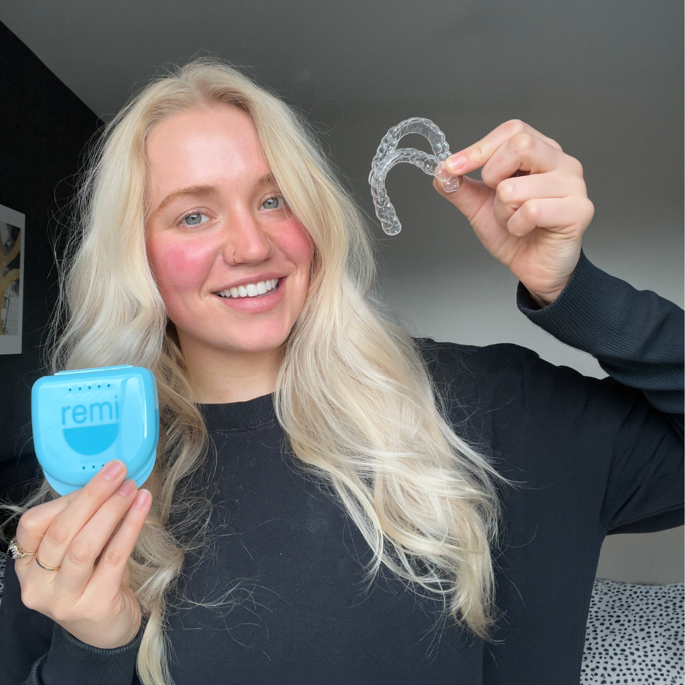 Woman holding a clear aligner and blue case with 'remi' branding.