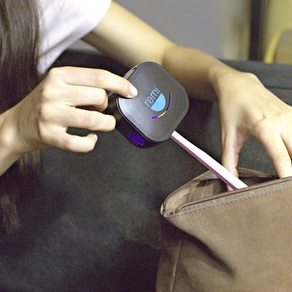 A person places a small black device labeled remi with a pink handle into a brown bag, suggesting portability and convenience—ideal for on-the-go hygiene with this UV toothbrush sanitizer.