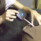 A person places a small black device labeled remi with a pink handle into a brown bag, suggesting portability and convenience—ideal for on-the-go hygiene with this UV toothbrush sanitizer.