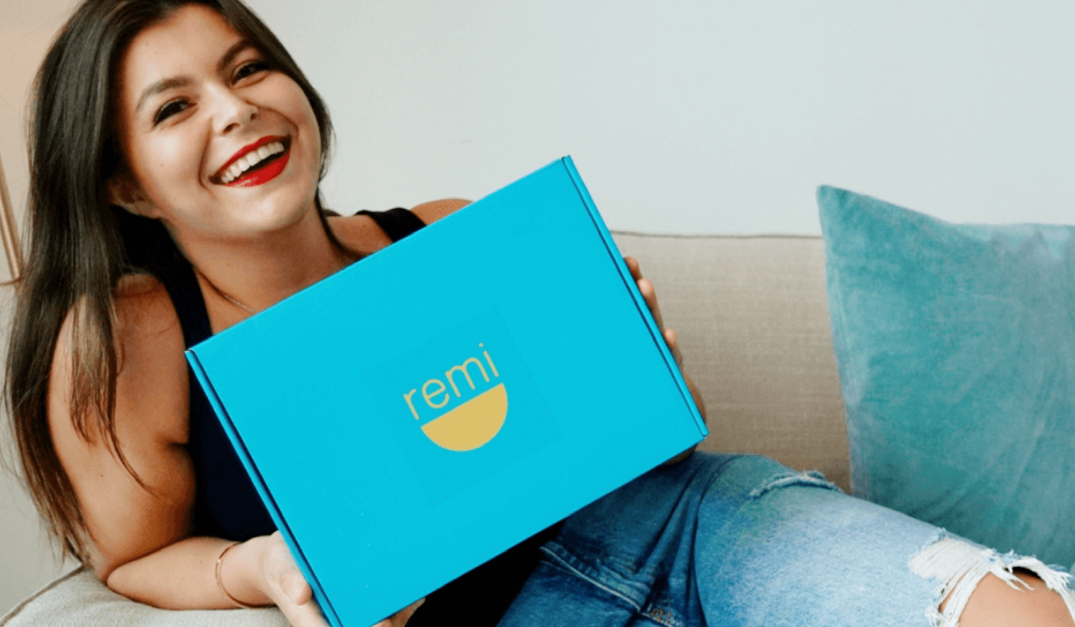 Woman smiling while holding a blue box with the logo "remi" on it.