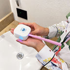 A person holds a white, square-shaped device labeled remi that emits blue light onto a pink toothbrush for plaque removal, above a bathroom sink.