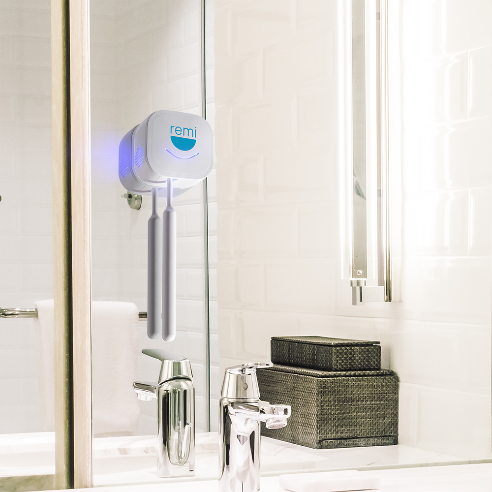 The Violife UV toothbrush sanitizer mounted on a bathroom mirror, illuminating with a blue light above a sink and toiletries.